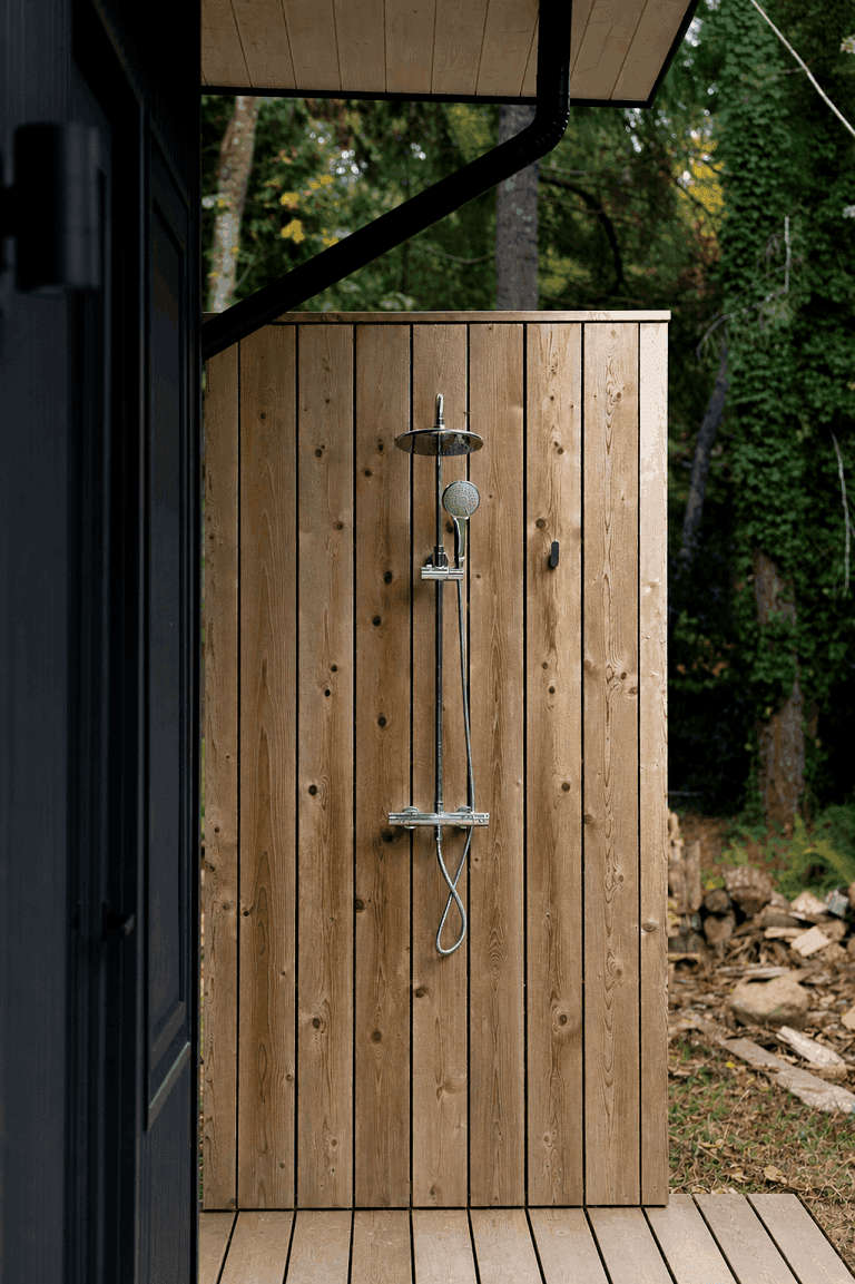 Outdoor cedar shower with a chrome rain shower head, opening onto the forest edge