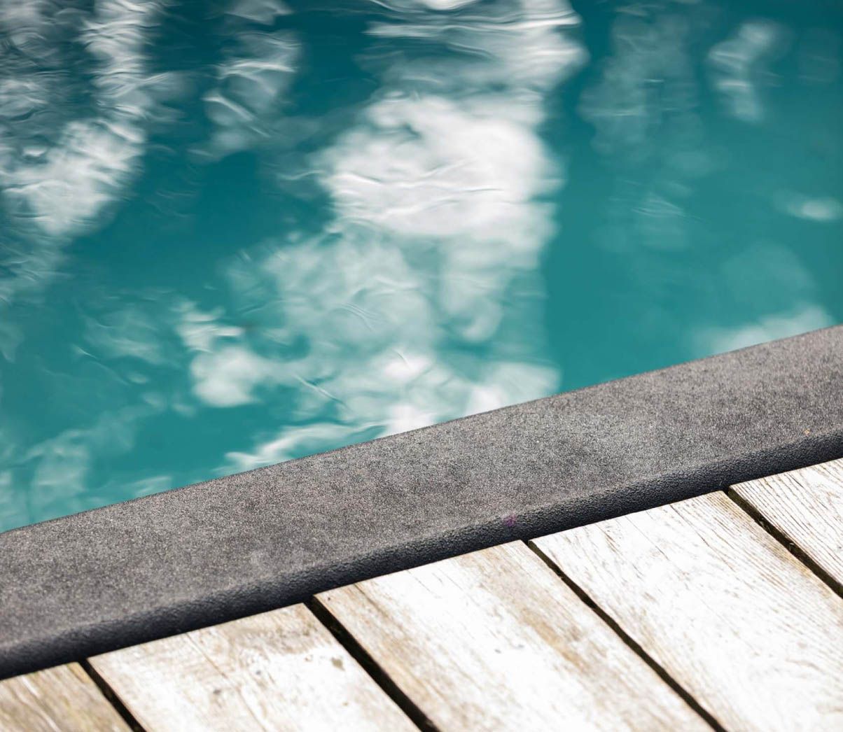 Detail of the dark stone coping meeting the weathered cedar deck at the water's edge