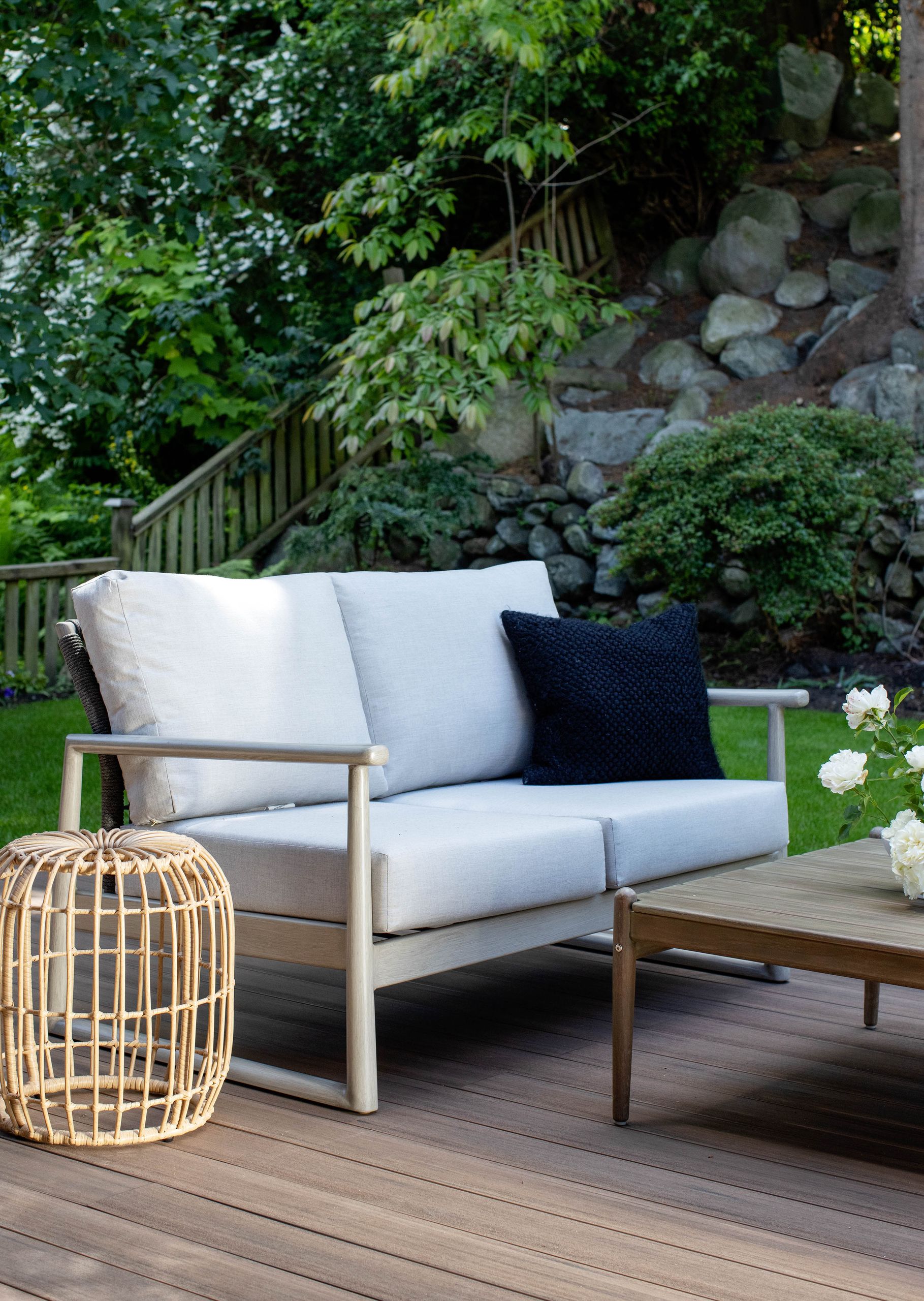 Deck sofa and rattan side stool below the planted rock slope