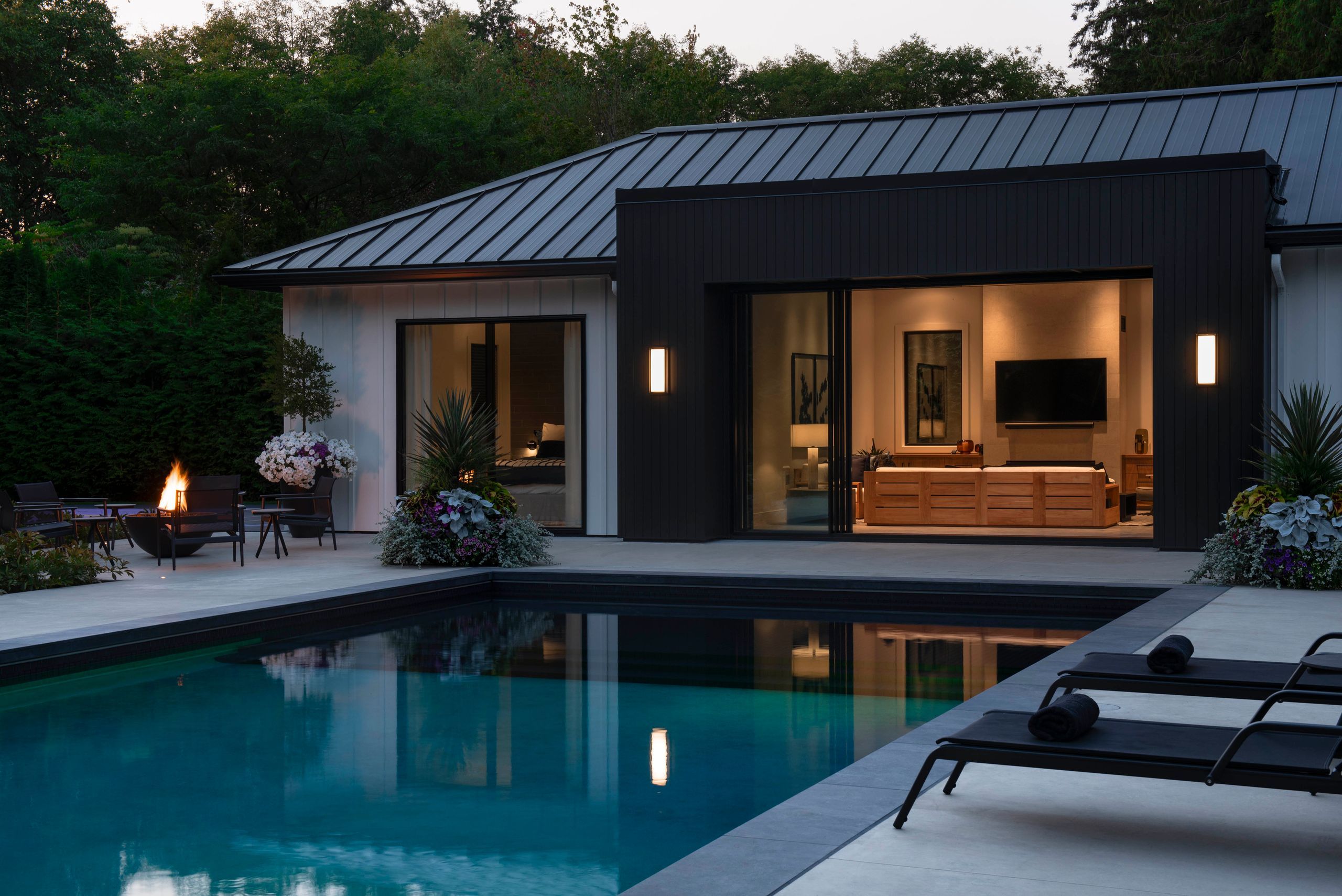 Pool house and terrace at dusk, with a lit fire bowl beside the pool