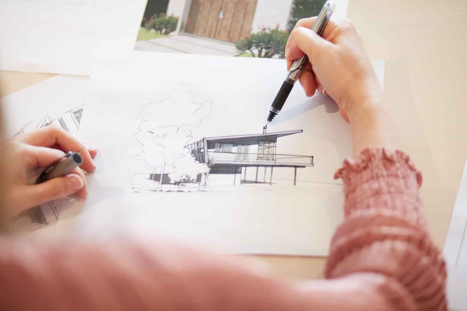 Hands sketching a house elevation in ink over a site photograph