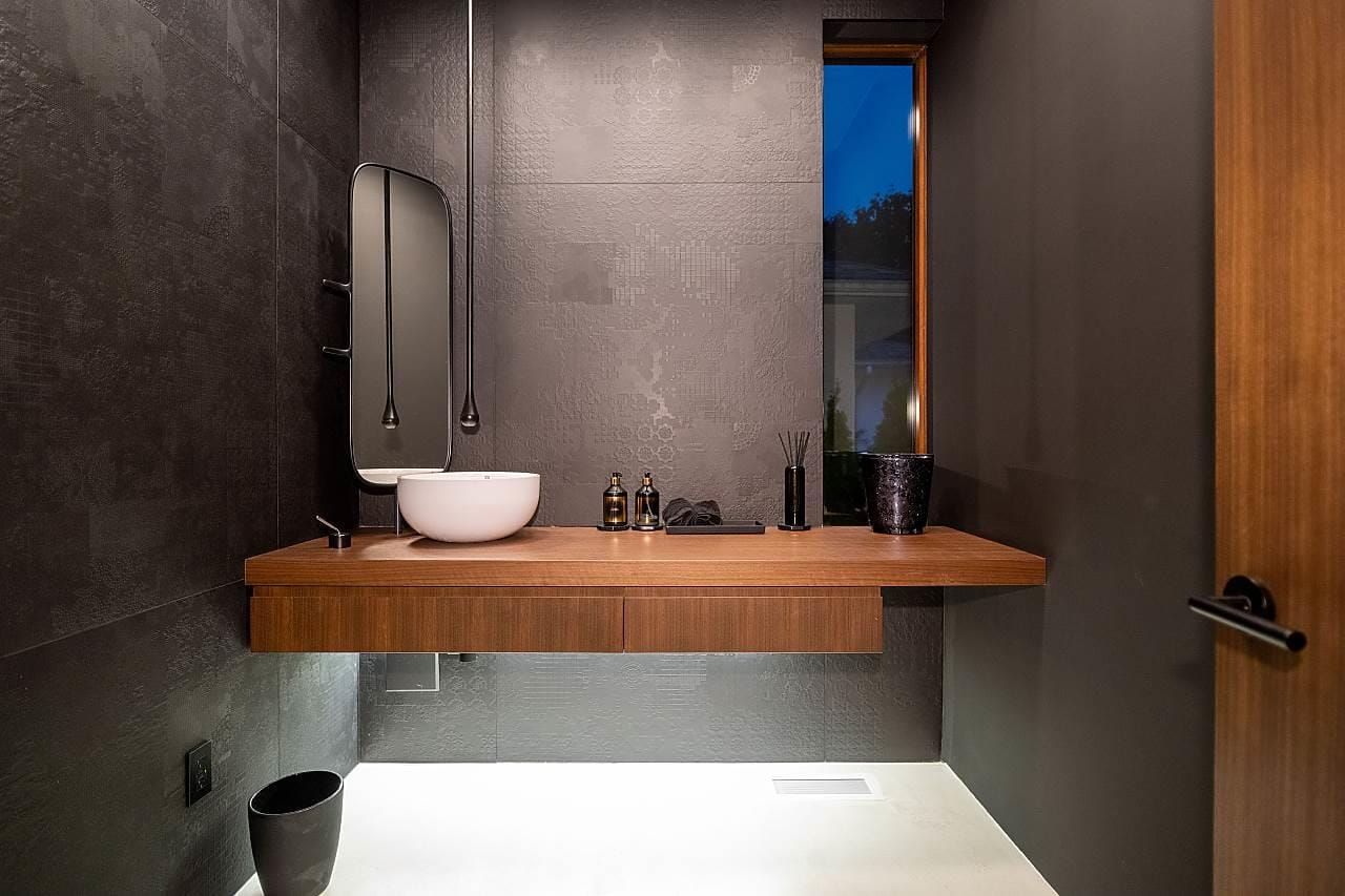 Powder room with a walnut floating vanity and a white vessel basin on dark tile
